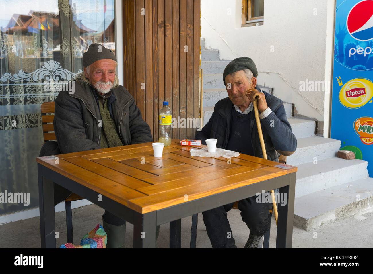 Due uomini anziani che hanno una conversazione rilassata e bevono limonata a un tavolo all'aperto, Sapanta, Sapanta, Maramures, Maramures, Maramuresh, Romania Foto Stock