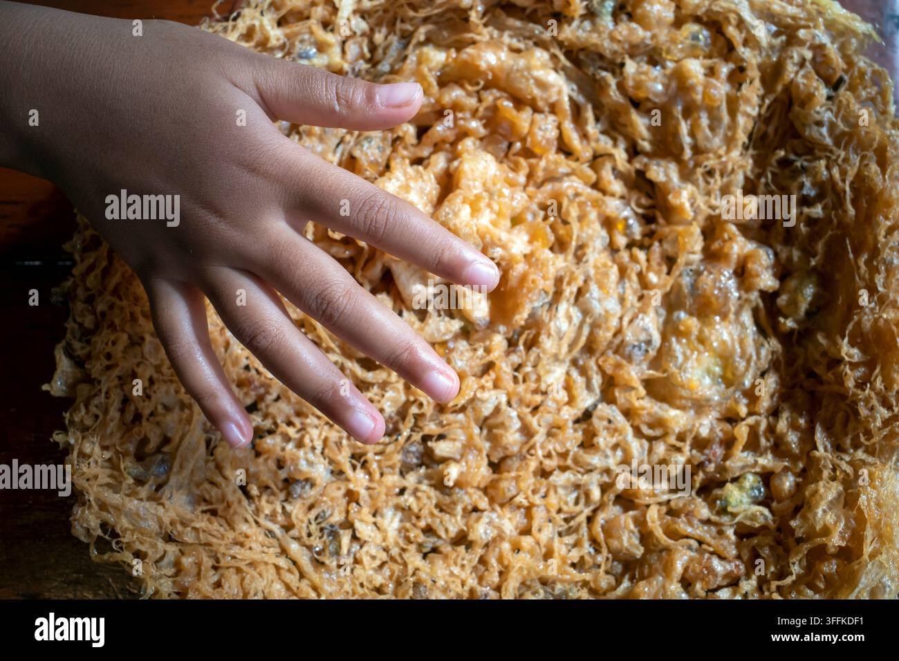 Primo piano della mano di un bambino che tocca una grande frittata dorata e croccante, evidenziando le sue dimensioni e la texture croccante. Foto Stock