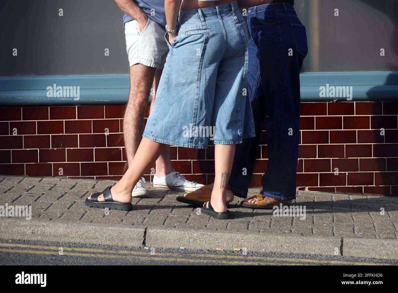Interazione sociale e stile di vita urbano, un gruppo di amici in piedi insieme su un marciapiede cittadino in abiti estivi casual. Persone che indossano shorts di jeans a Foto Stock