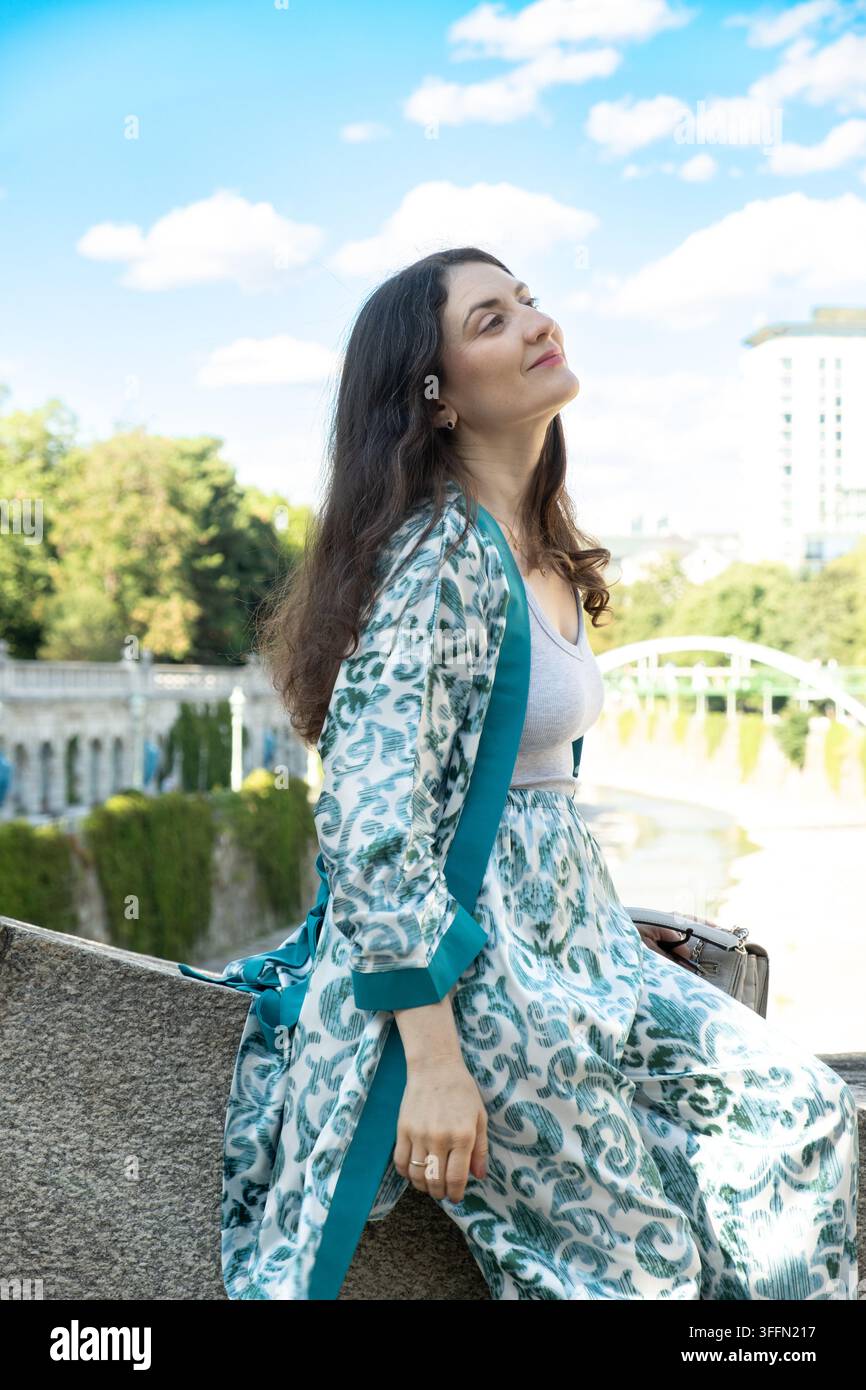 Bella donna bruna adulta seduta all'aperto in un parco cittadino Foto Stock