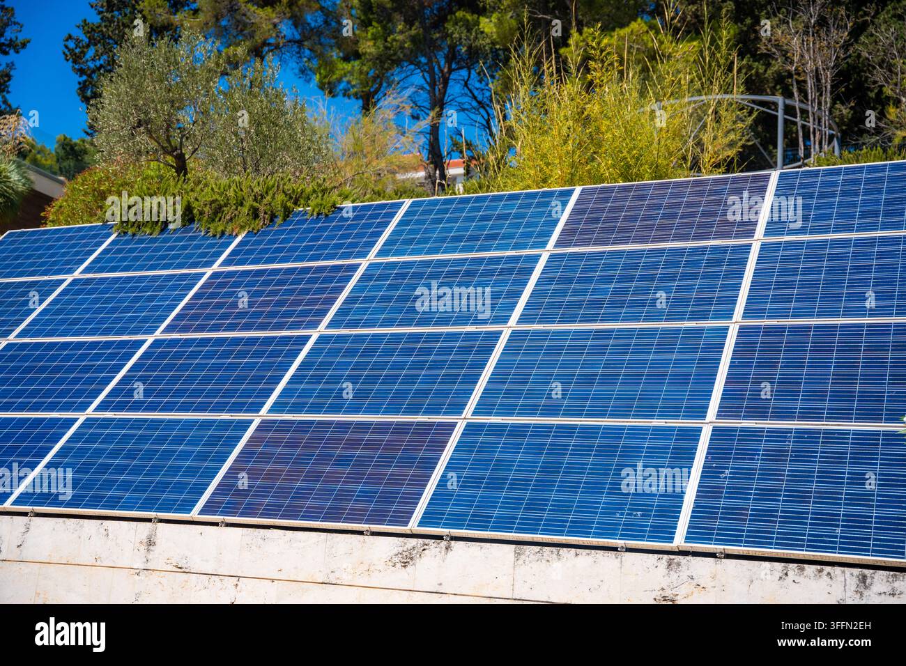 Pannelli solari installati su un tetto, che mostrano celle fotovoltaiche blu sotto la luce intensa del sole con vegetazione sullo sfondo, Croazia Foto Stock