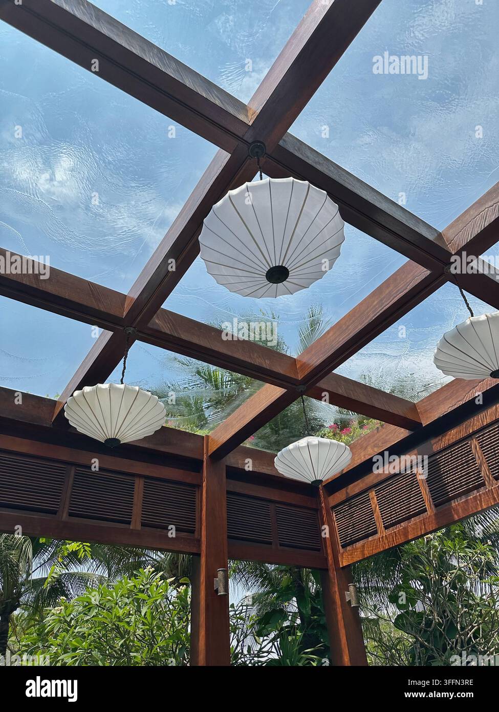 Lucernario di padiglione tropicale. Elegante padiglione in legno con tetto in vetro traslucido e lanterne di carta scultoree, circondato da una lussureggiante vegetazione tropicale ben Foto Stock