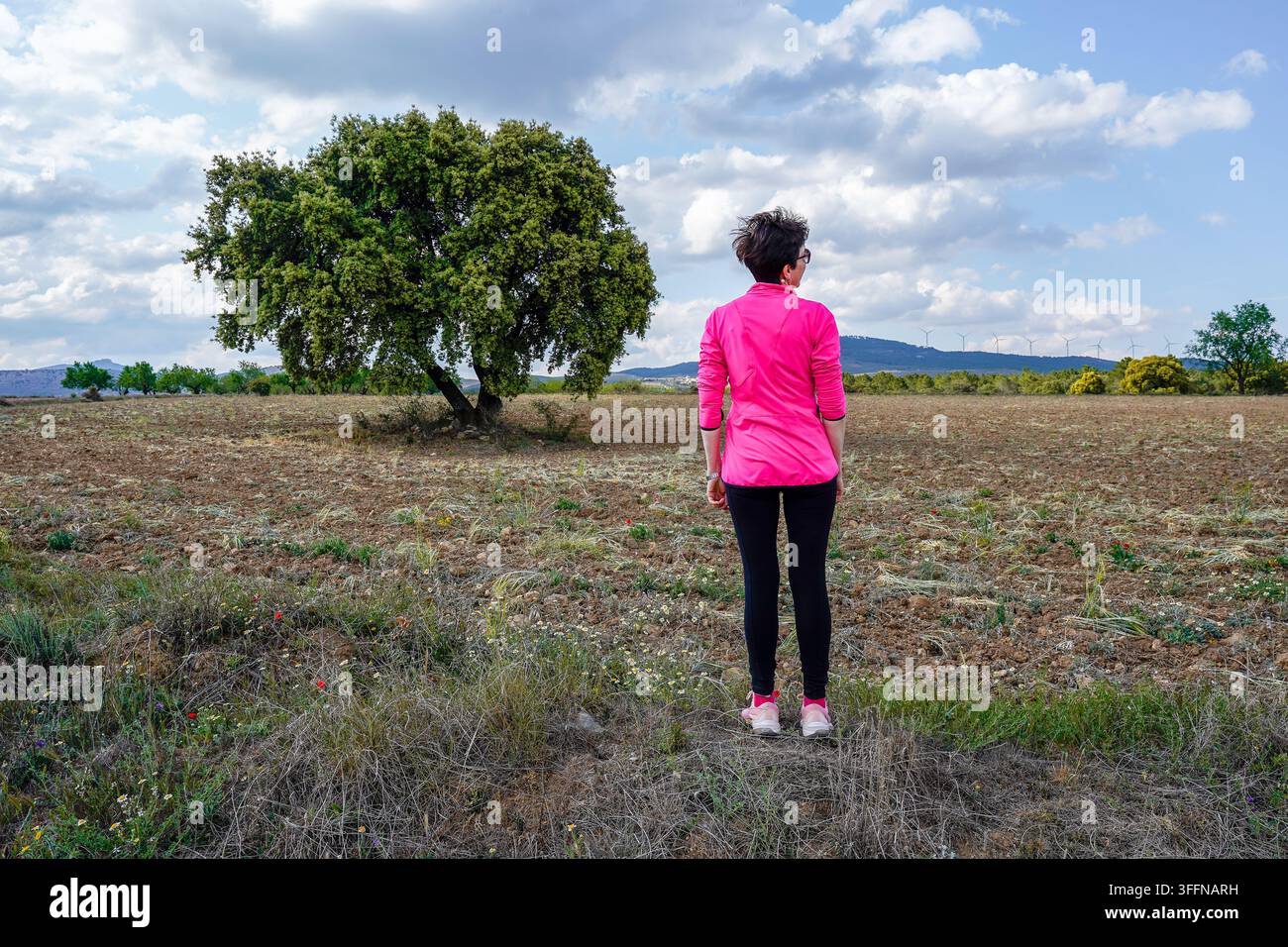 Donna in piedi in un campo che guarda il paesaggio, salva ricordi sul suo telefono cellulare Foto Stock