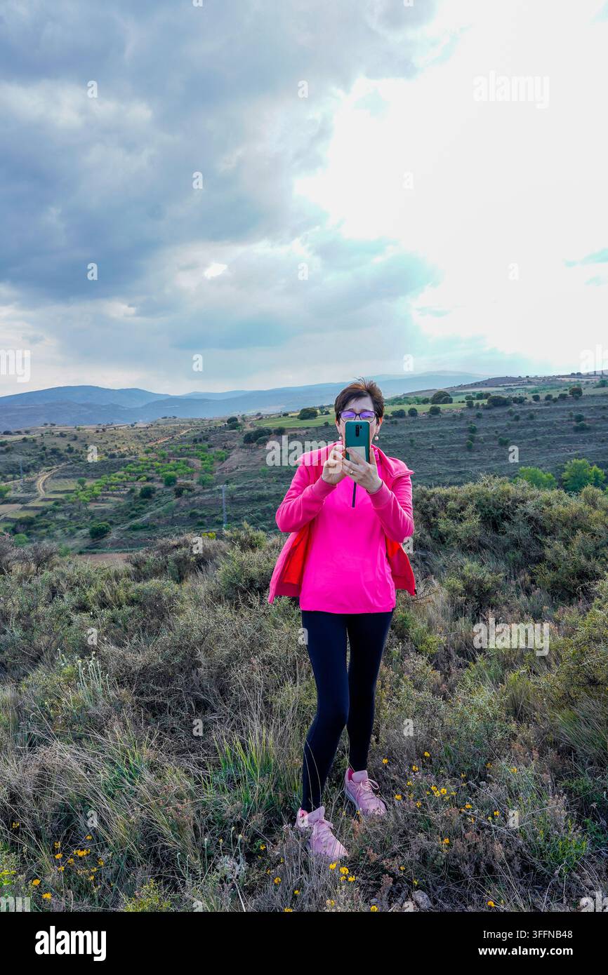 Donna in piedi su una collina che scatta foto del paesaggio naturale con il suo telefono Foto Stock
