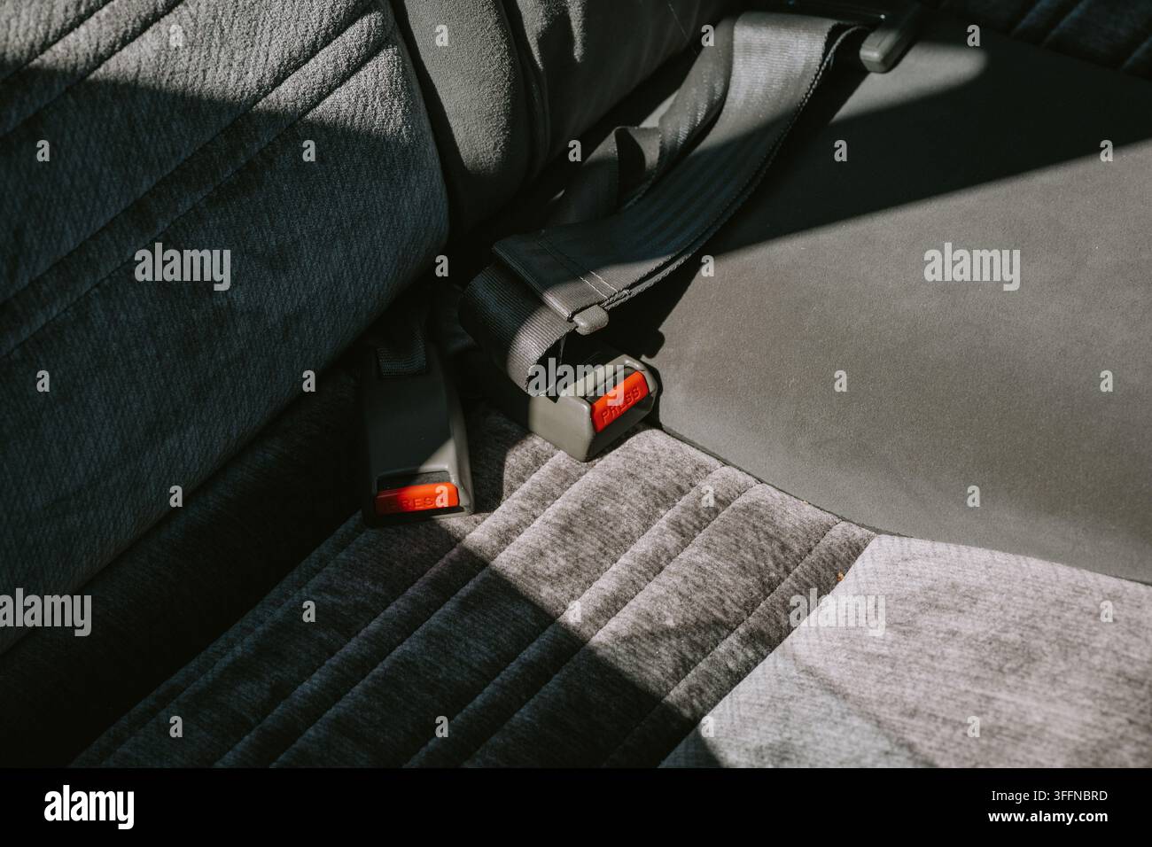 Vista ravvicinata dettagliata della tappezzeria in velluto grigio felpato e delle fibbie delle cinture di sicurezza sul sedile posteriore di un'automobile vintage. Foto Stock