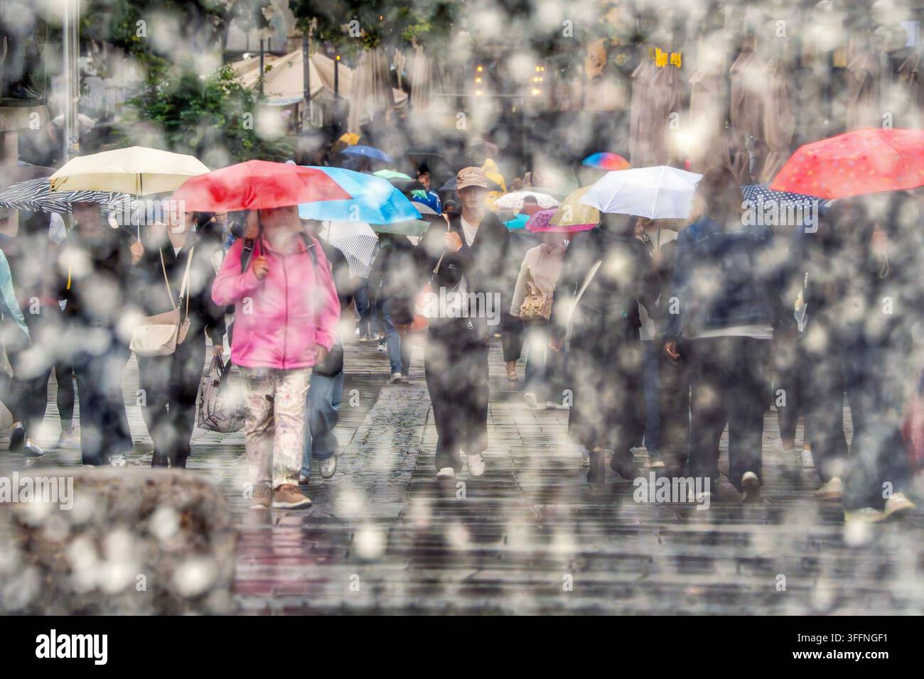 Shopping sotto la pioggia, passanti con ombrelli nella zona pedonale, fotografati simbolicamente attraverso le fontane della fontana Stachus, sembra già che sia autunno con temperature intorno ai 16 gradi, Monaco di Baviera, settembre 2026 Germania, Monaco di Baviera, settembre 2026, Shopping sotto la pioggia, passanti con ombrelli nella zona pedonale, fotografati attraverso le fontane della fontana Stachus, il muro di gocce d'acqua getta un velo sulla scena, sembra già che sia autunno con tempo piovoso a 16 gradi, i colori mettono accenti luminosi nel tempo piovoso grigio, mercoledì pomeriggio verso le 15, Einze Foto Stock