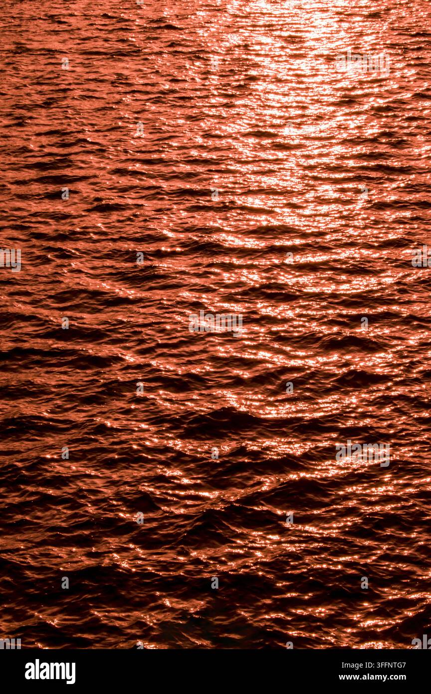 Acqua increspata con luce calda, dorata-rossa che si riflette sulle piccole onde al tramonto Foto Stock