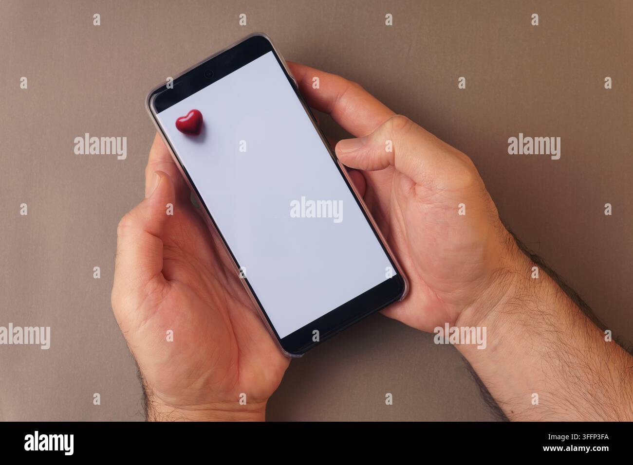 Primo piano di mani maschili che tengono un modello di telefono cellulare. Concetto di messaggio digitale per San Valentino, appuntamenti online o modello di app romantica. Foto Stock