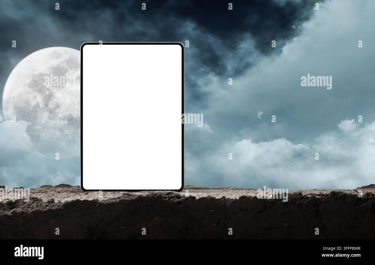 Dispositivo tablet vuoto in piedi su terra scura contro un cielo notturno spettrale con luna piena Foto Stock