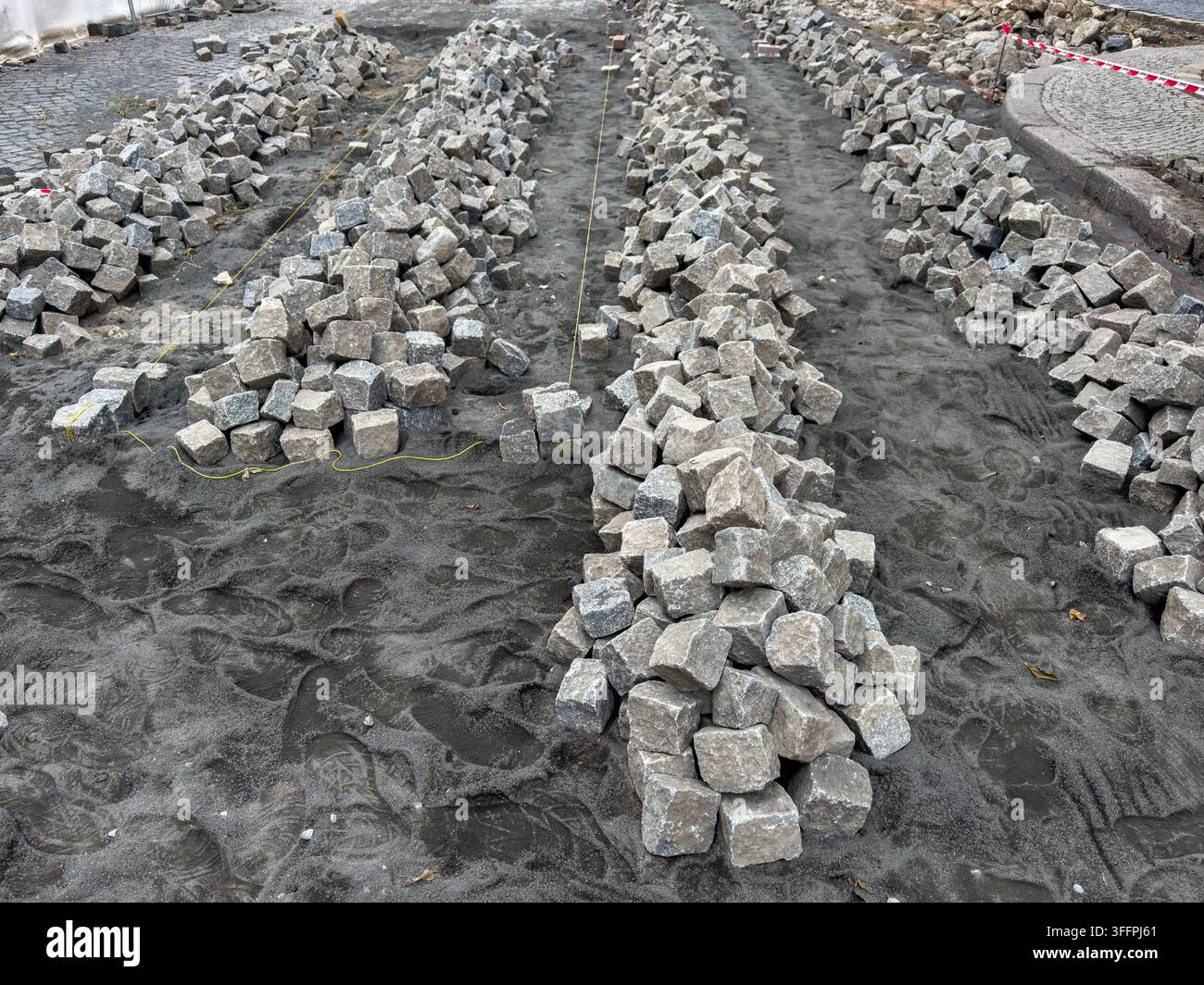 File di pietre di granito grigio e ciottoli impilati su un cantiere edile sabbioso. processo di ricostruzione stradale, lavori di ristrutturazione della strada, urbano Foto Stock