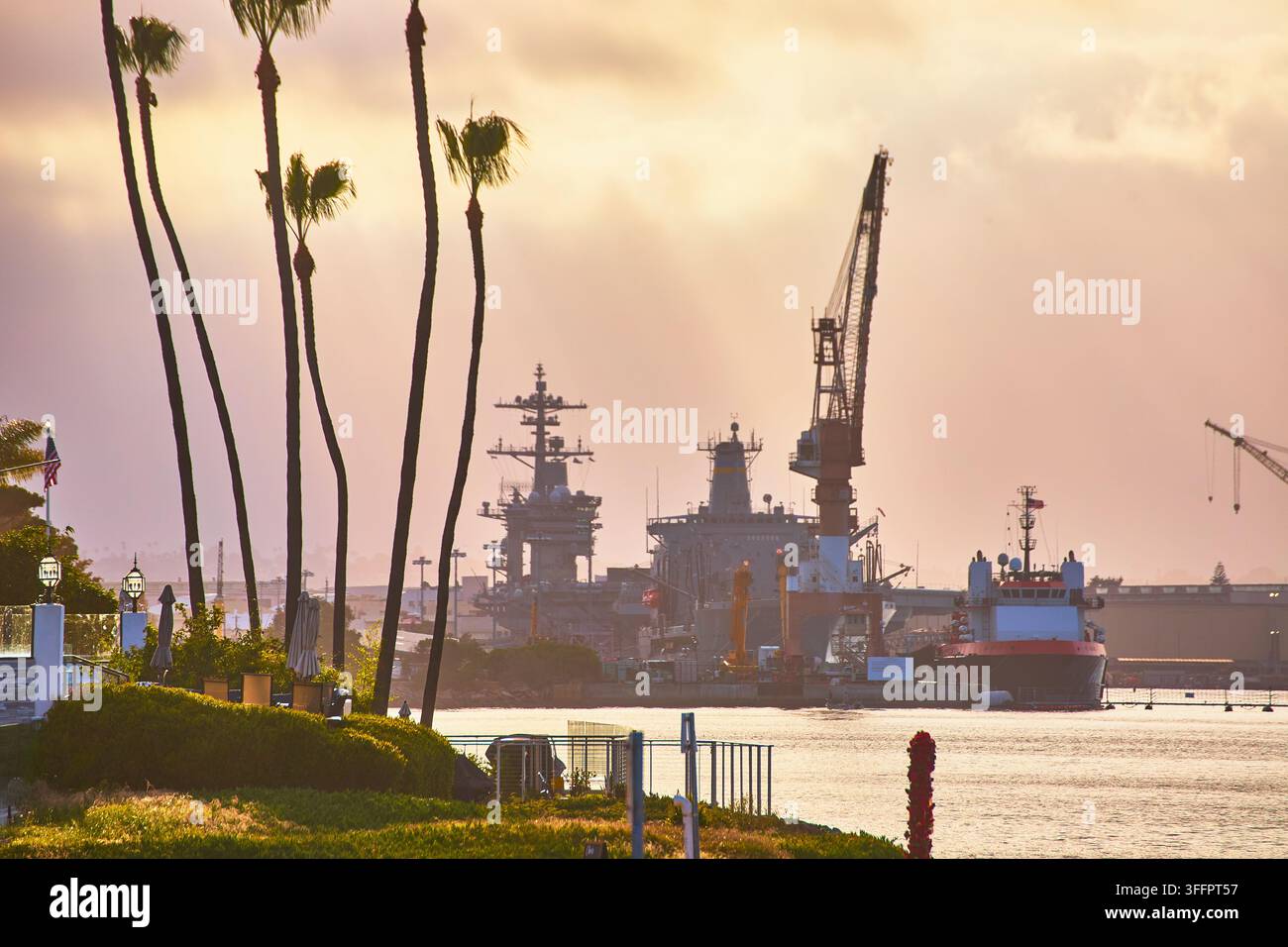 Le palme costeggiano il bordo della Baia di San Diego mentre navi della marina e militari attraccano sotto il cielo dorato dell'ora dorata. L'atmosfera pacifica evidenzia il blu unico Foto Stock