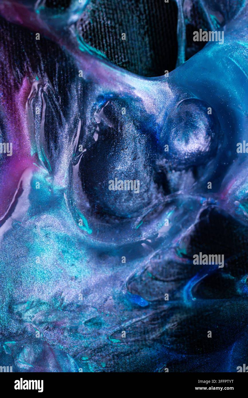 Composizione astratta in primo piano di fluido blu, viola e nero vorticante con particelle di glitter scintillanti, che creano una texture cosmica eterea e dra… Foto Stock
