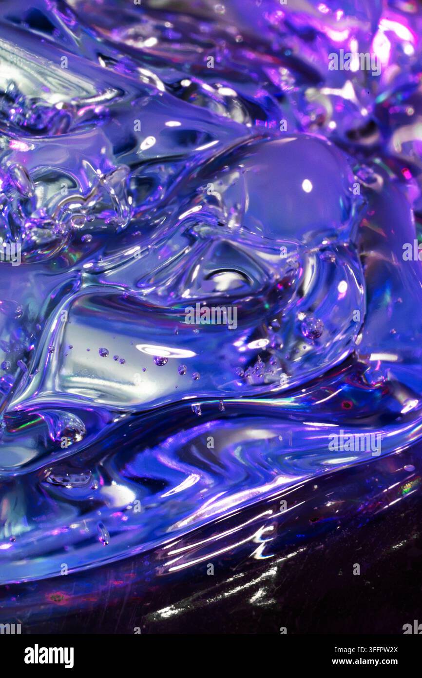 Composizione astratta in primo piano di vetro traslucido lucido con riflessi iridescenti viola, blu e argento, che creano forme fluide e punti luce luminosi Foto Stock
