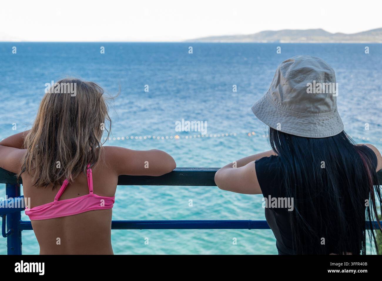 Due donne si appoggiano a una ringhiera e guardano il mare blu e calmo. Foto Stock