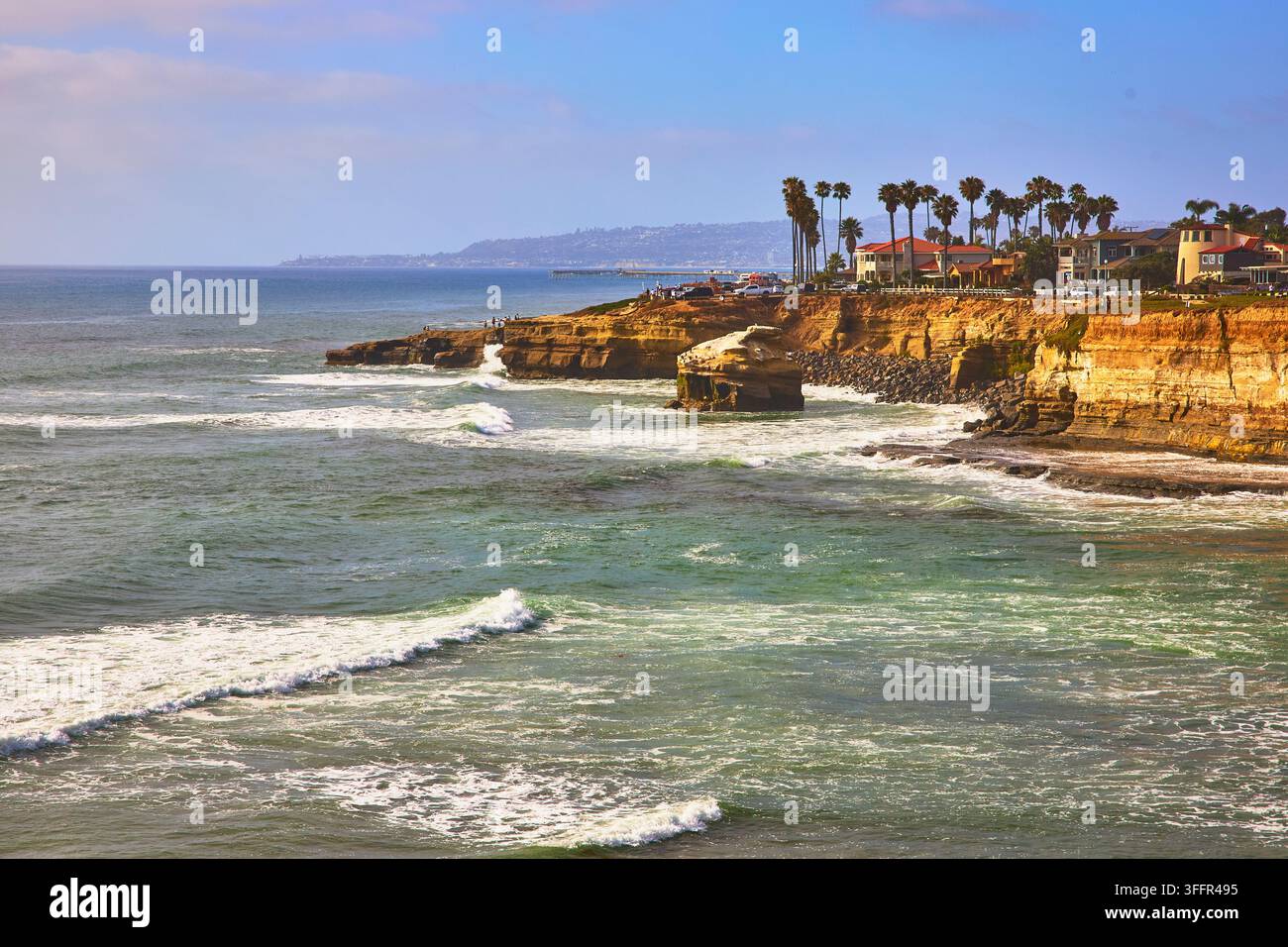 Le onde dell'oceano si infrangono contro le iconiche scogliere di arenaria delle Sunset Cliffs a San Diego in California, mentre palme e case eleganti si affacciano sullo scenario panoramico Foto Stock