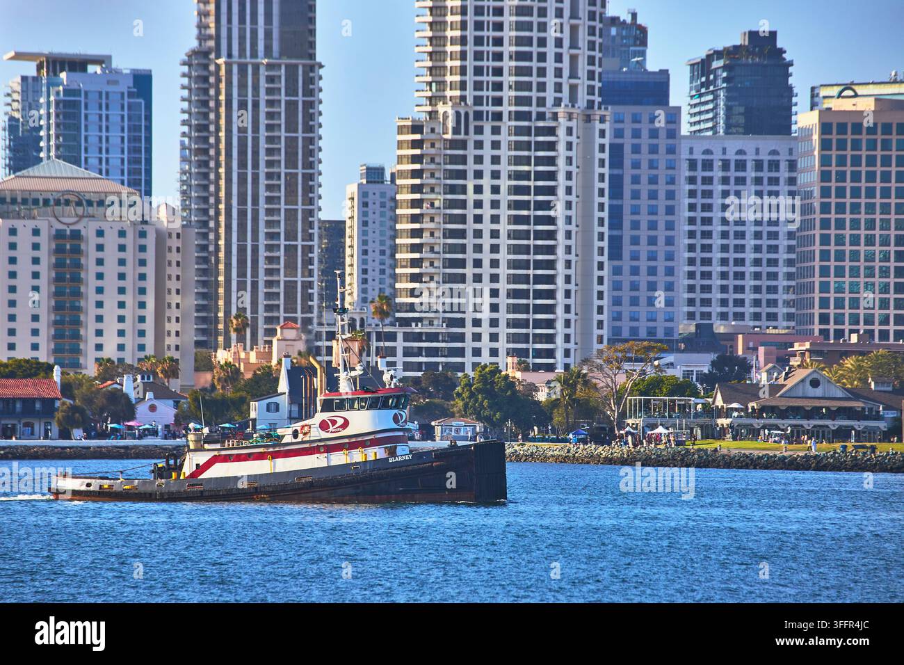 Una nave classica scivola attraverso la baia di San Diego in California con lo skyline della città che si staglia alle spalle. Il lungomare vibra di attività mentre archi moderni Foto Stock