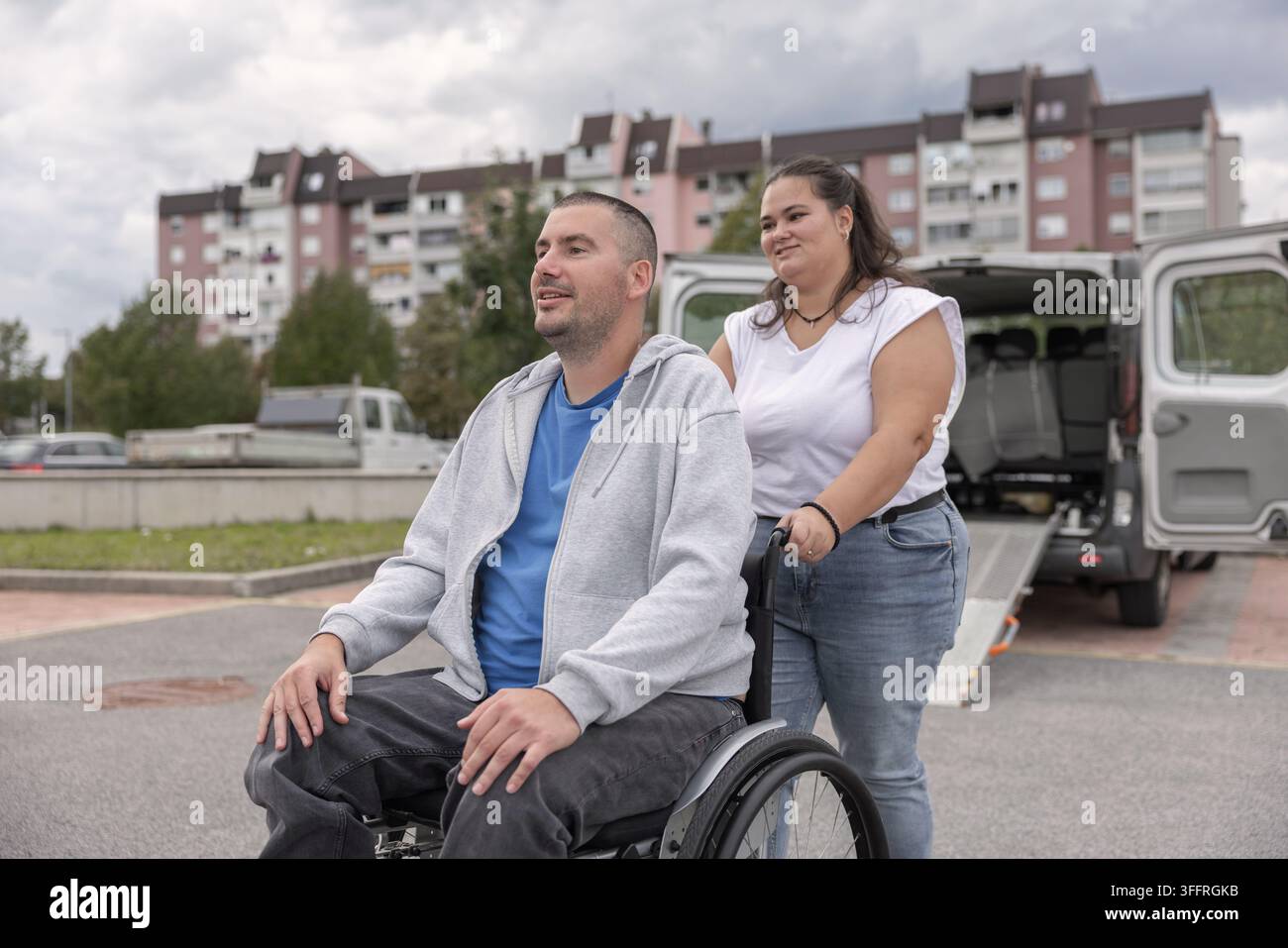 Utente di sedia a rotelle manuale che si gode una passeggiata all'aperto con un'assistente personale mentre chiacchiera, sorride e trascorre del tempo di qualità insieme. Foto Stock