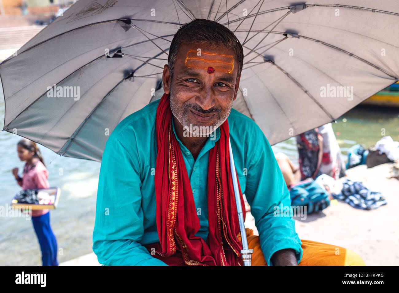 Uomo indiano in abiti tradizionali seduto sotto un ombrellone Foto Stock