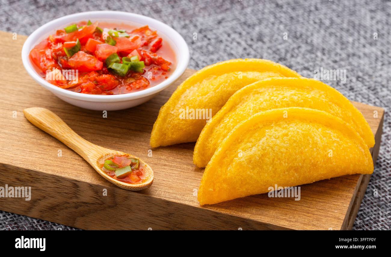 Empanadas di mais colombiani precotti, presentati su una tavola di legno con salsa hogao tradizionale. Foto Stock