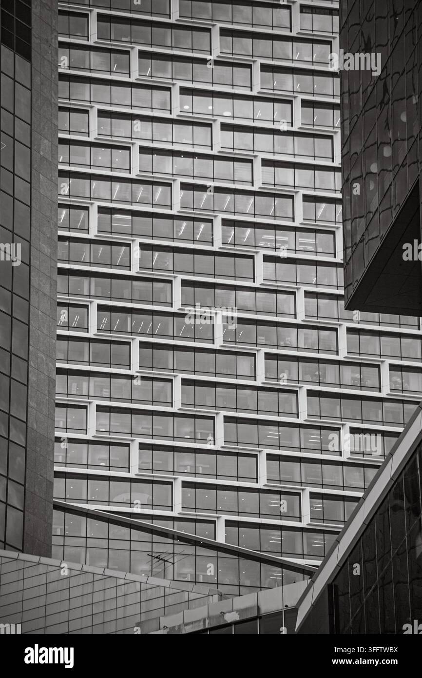 Scena urbana in bianco e nero con un grande torre per uffici e cornici di finestre a forma di scatola sfalsate tra altri edifici vetrati. Foto Stock