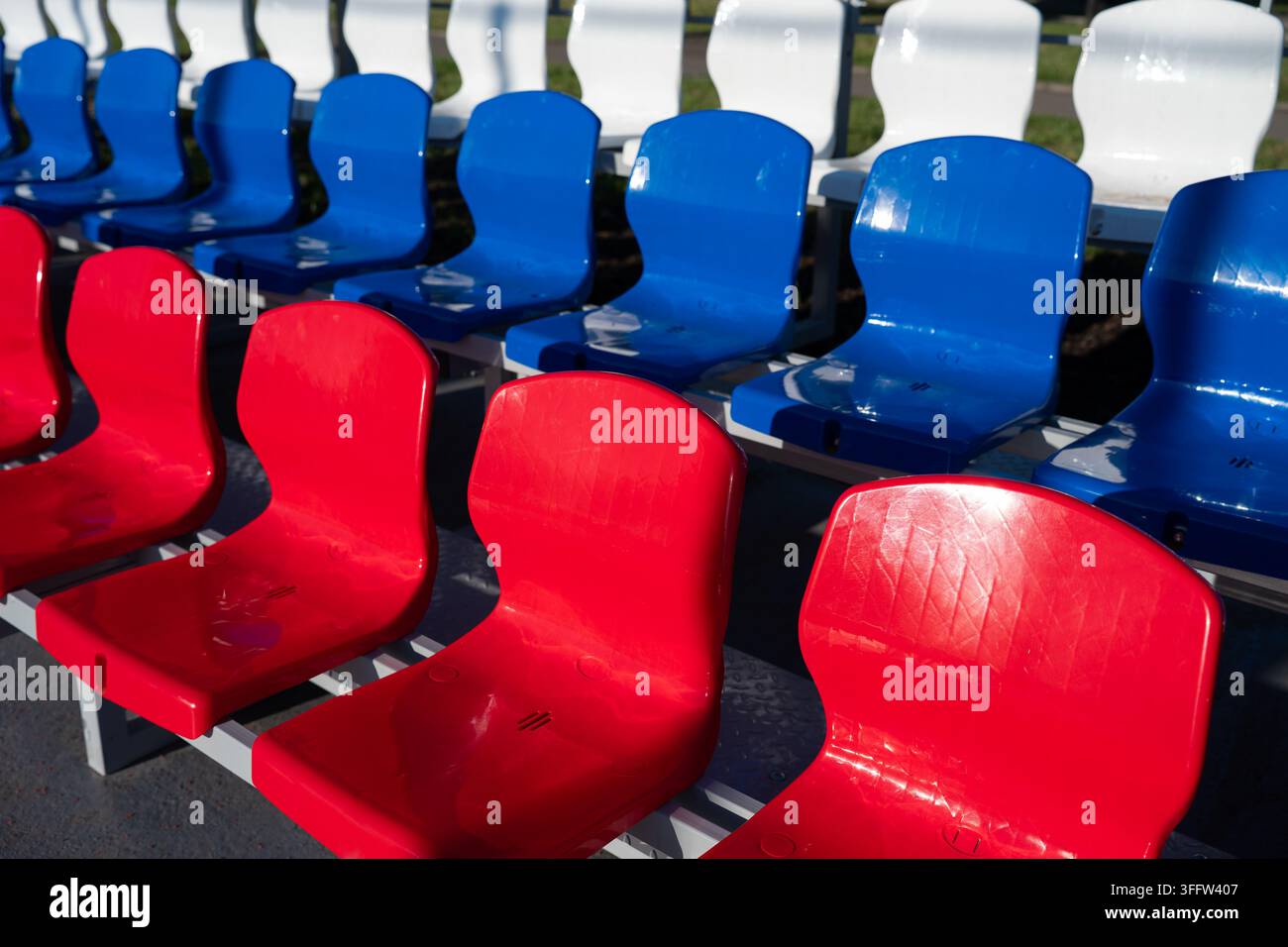 Sfondo astratto con sedie da stadio in plastica rosse, blu e bianche. File di sedie colorate in plastica in una tribuna moderna di un'arena sportiva. Foto Stock