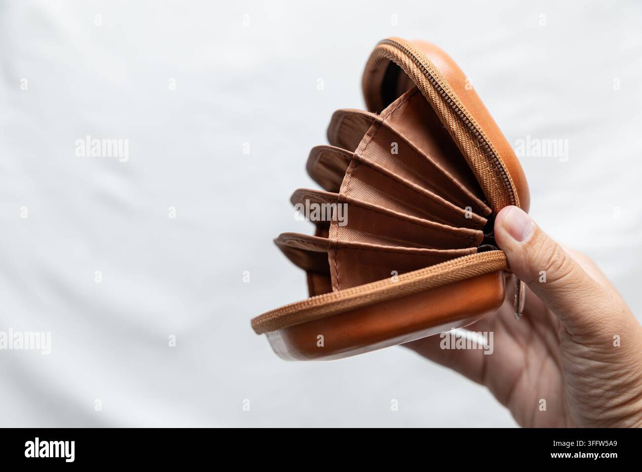 Mano che tiene aperto un organizer marrone con cerniera, con più scomparti e interno strutturato su sfondo chiaro con spazio per il testo. Foto Stock