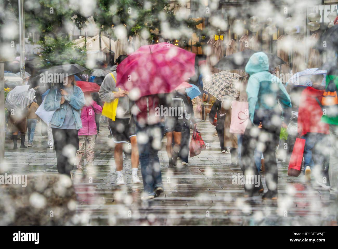 Shopping sotto la pioggia, passanti con ombrelli nella zona pedonale, fotografati simbolicamente attraverso le fontane della fontana Stachus, sembra già che sia autunno con temperature intorno ai 16 gradi, Monaco di Baviera, settembre 2026 Germania, Monaco di Baviera, settembre 2026, Shopping sotto la pioggia, passanti con ombrelli nella zona pedonale, fotografati attraverso le fontane della fontana Stachus, il muro di gocce d'acqua getta un velo sulla scena, sembra già che sia autunno con tempo piovoso a 16 gradi, i colori mettono accenti luminosi nel tempo piovoso grigio, mercoledì pomeriggio verso le 15, Einze Foto Stock