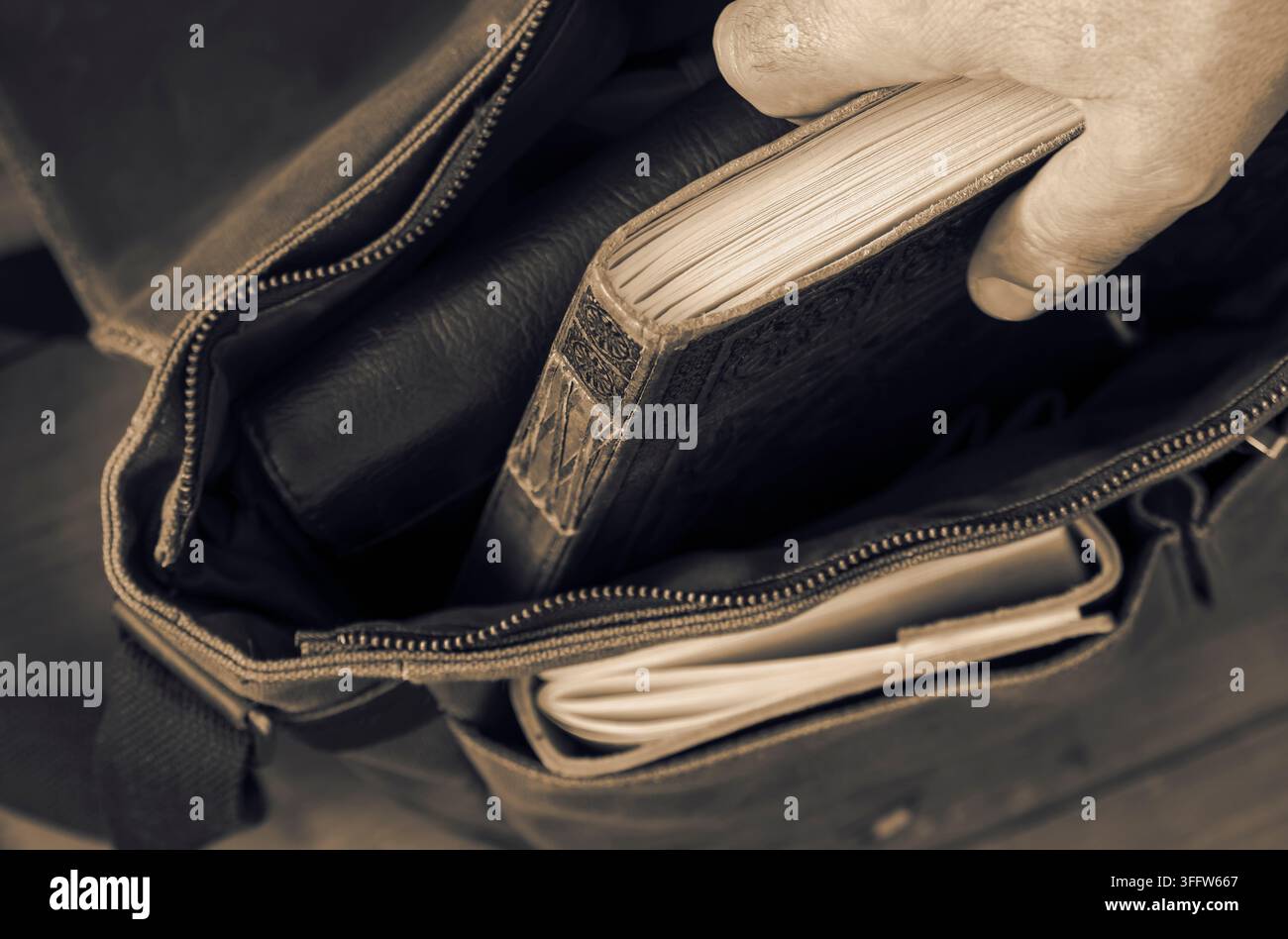 Uomo che estrae un diario in pelle vintage da una borsa a tracolla in tela verde. Su uno sfondo di pavimento in legno. Foto Stock