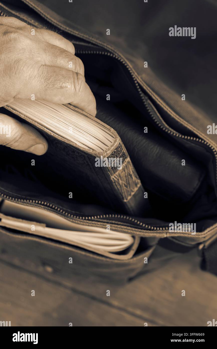 Uomo che estrae un diario in pelle vintage da una borsa a tracolla in tela verde. Su uno sfondo di pavimento in legno. Foto Stock