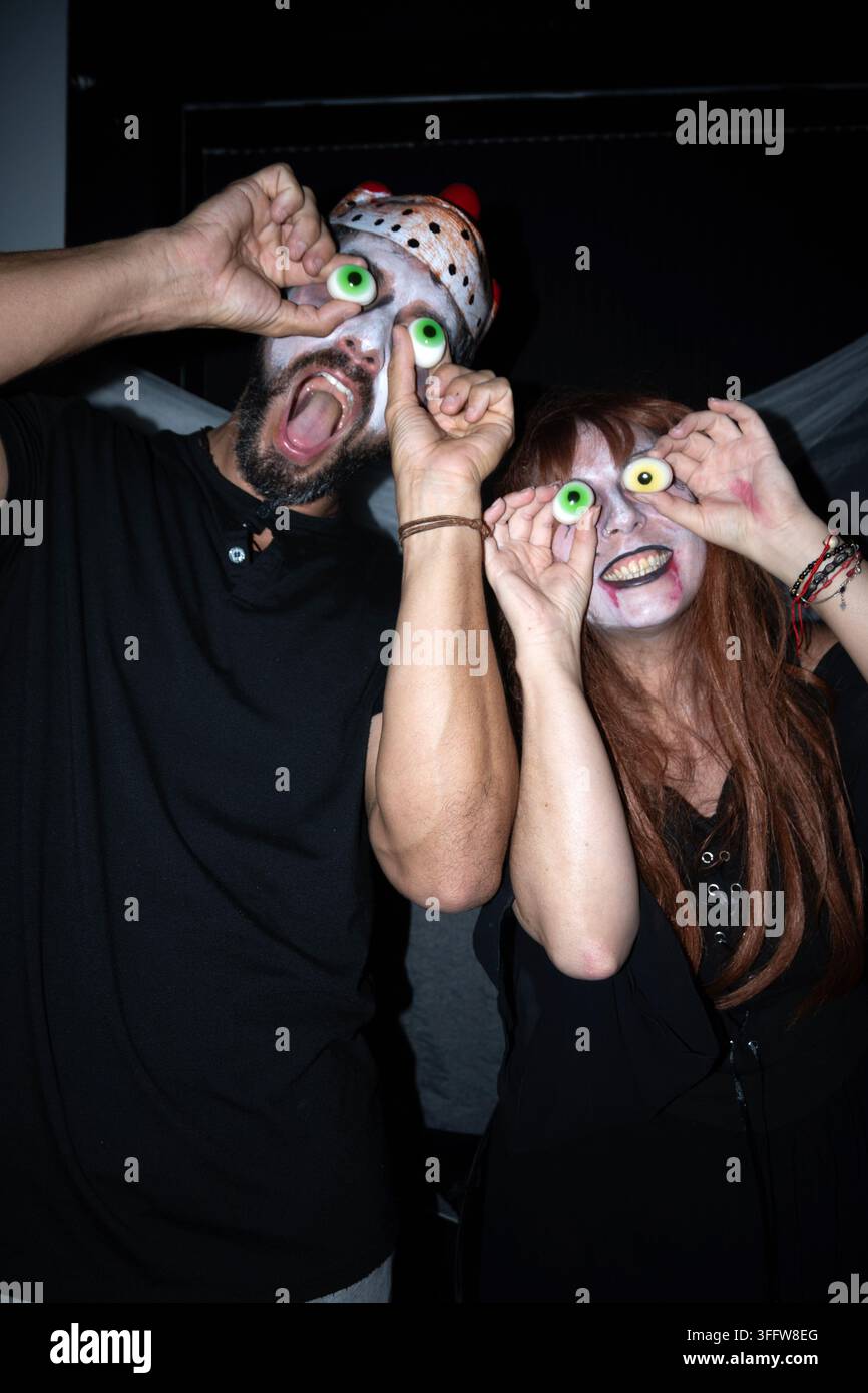 Uomo e donna in costumi di Halloween che tengono occhi di caramelle sopra i loro occhi e fanno espressioni divertenti a una festa. Foto Stock