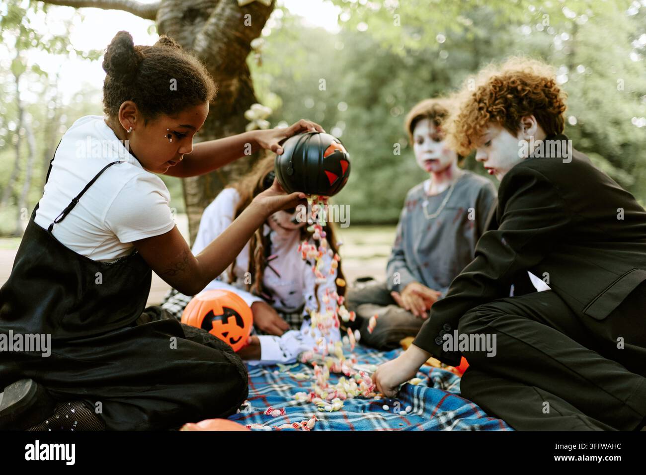 Bambini multietnici che versano caramelle di Halloween da un secchio nel parco Foto Stock