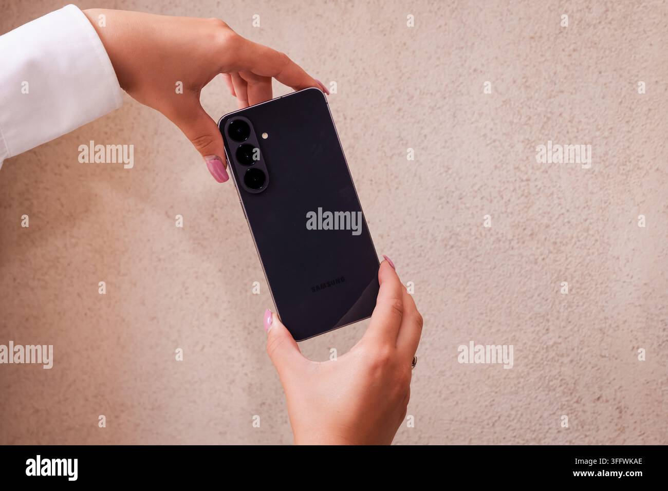 RIGA, LETTONIA. 25 agosto 2026. Persona che tiene il smartphone Samsung Galaxy S26 FE con entrambe le mani per presentare il design elegante del retro e la parte posteriore opaca Foto Stock