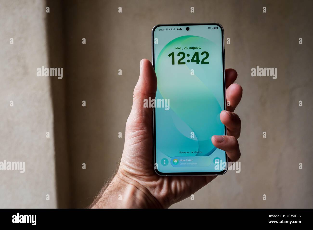RIGA, LETTONIA. 25 agosto 2026. Mano che tiene il Samsung Galaxy S26 FE verde chiaro che mostra lo sfondo dello schermo di blocco con l'ora 12:42. Foto Stock