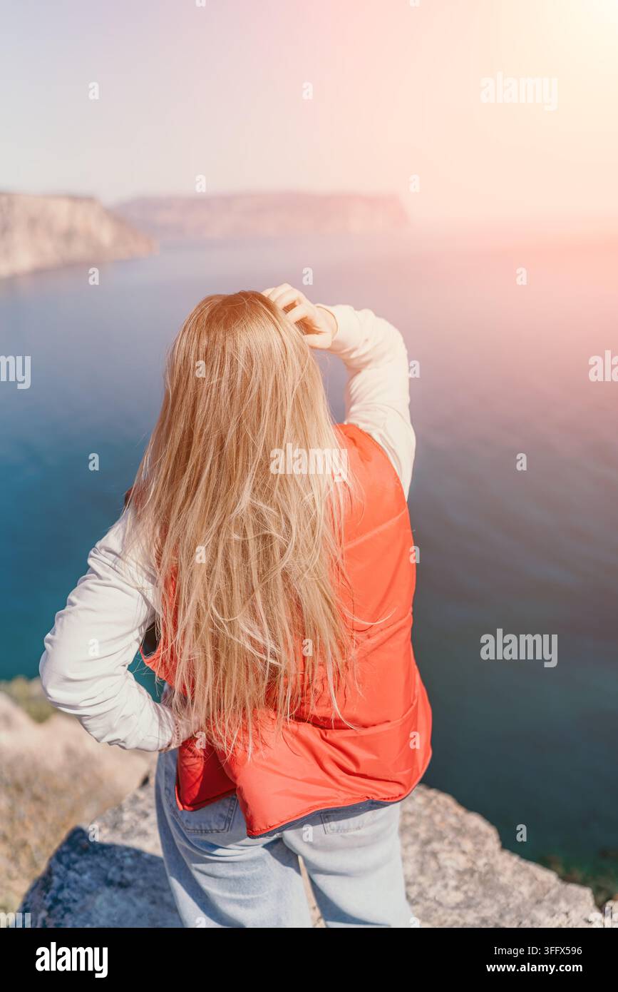 Donna su una scogliera sul mare, in piedi sul bordo di una montagna che guarda l'oceano durante il tramonto con spazio copia Foto Stock