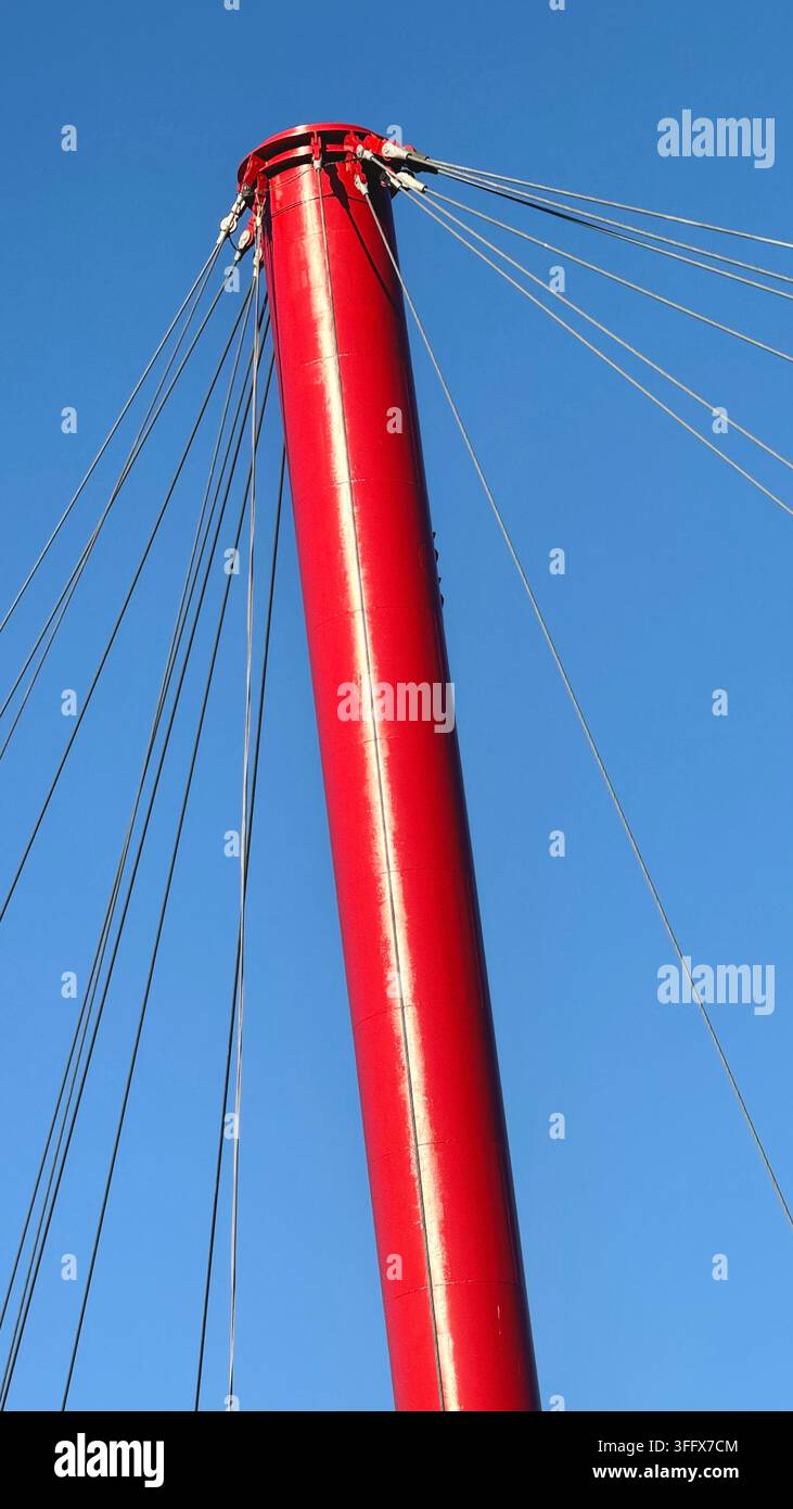 Prima vista di una struttura di ponte in acciaio rosso e dei cavi di sospensione contro un cielo blu chiaro, con ampio spazio negativo in una composizione minimalista Foto Stock