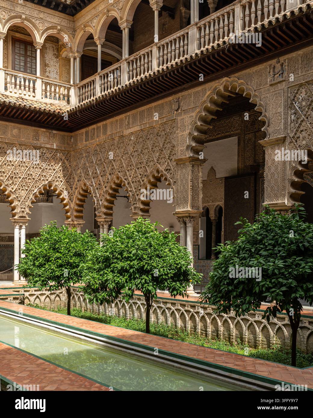 Piscina nel cortile reale delle Doncellas dell'Alcazar con un albero di arance e archi intagliati sopra colonne di marmo, Siviglia Foto Stock