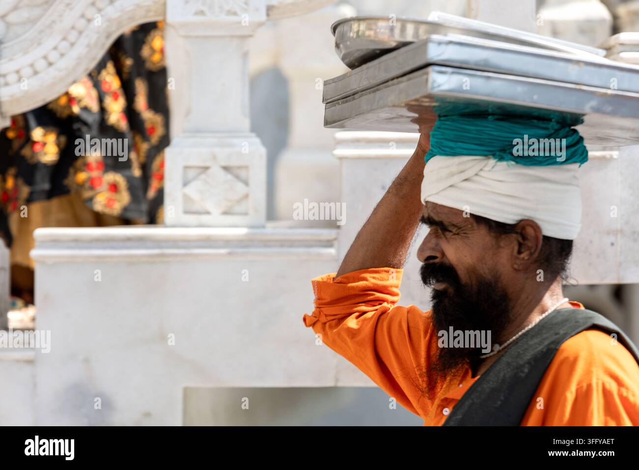 Uomo indiano che porta vassoio di metallo sulla testa in un tempio Foto Stock
