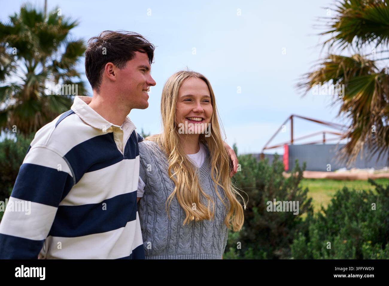 Giovane coppia sorridente che cammina insieme in una giornata soleggiata all'aperto. Foto Stock