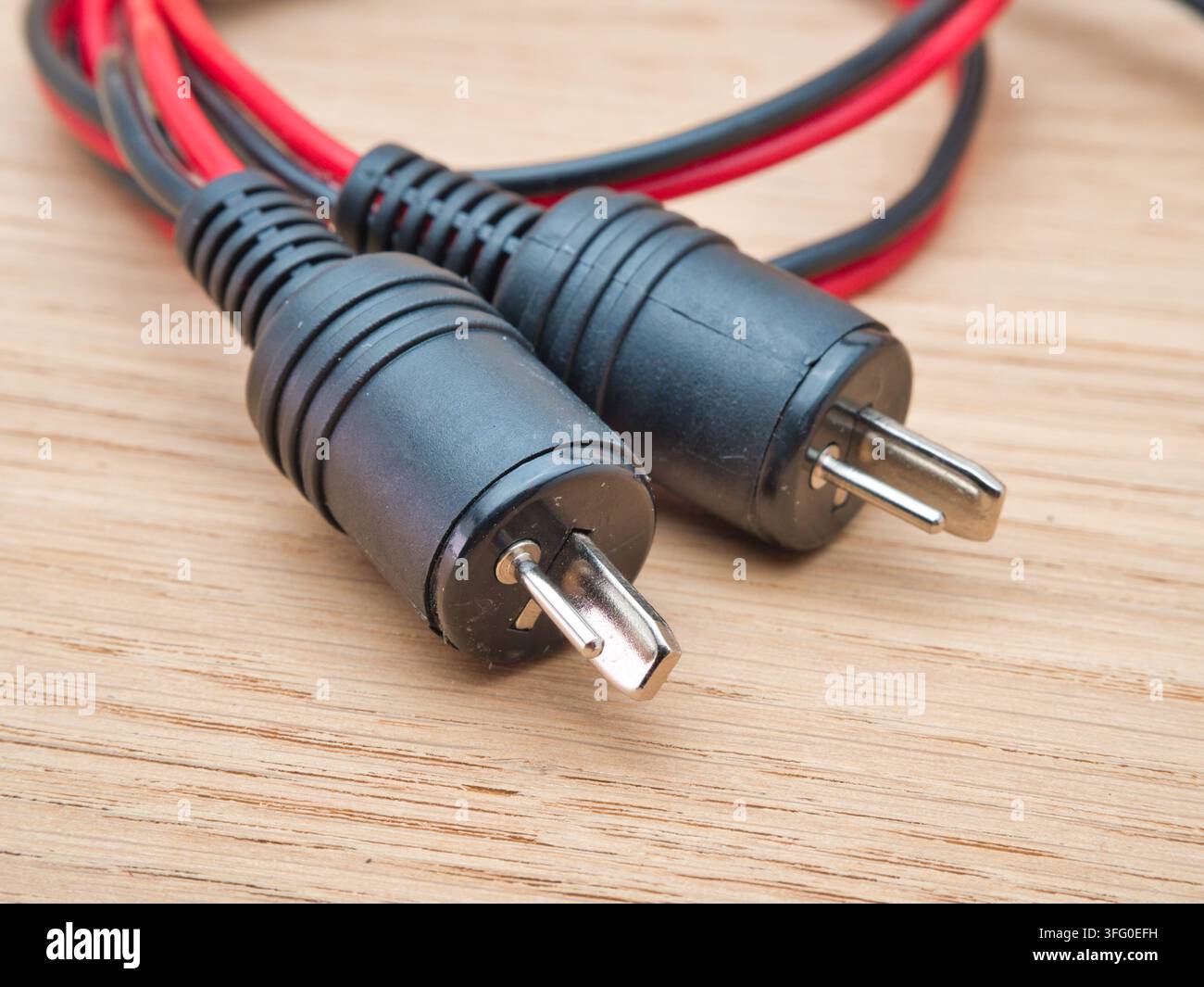 Connettori per cavo altoparlante RCA su legno - Una coppia di connettori per cavo altoparlante audio RCA neri e rossi con strisce di rame esposte riposa ordinatamente su un legno chiaro Foto Stock