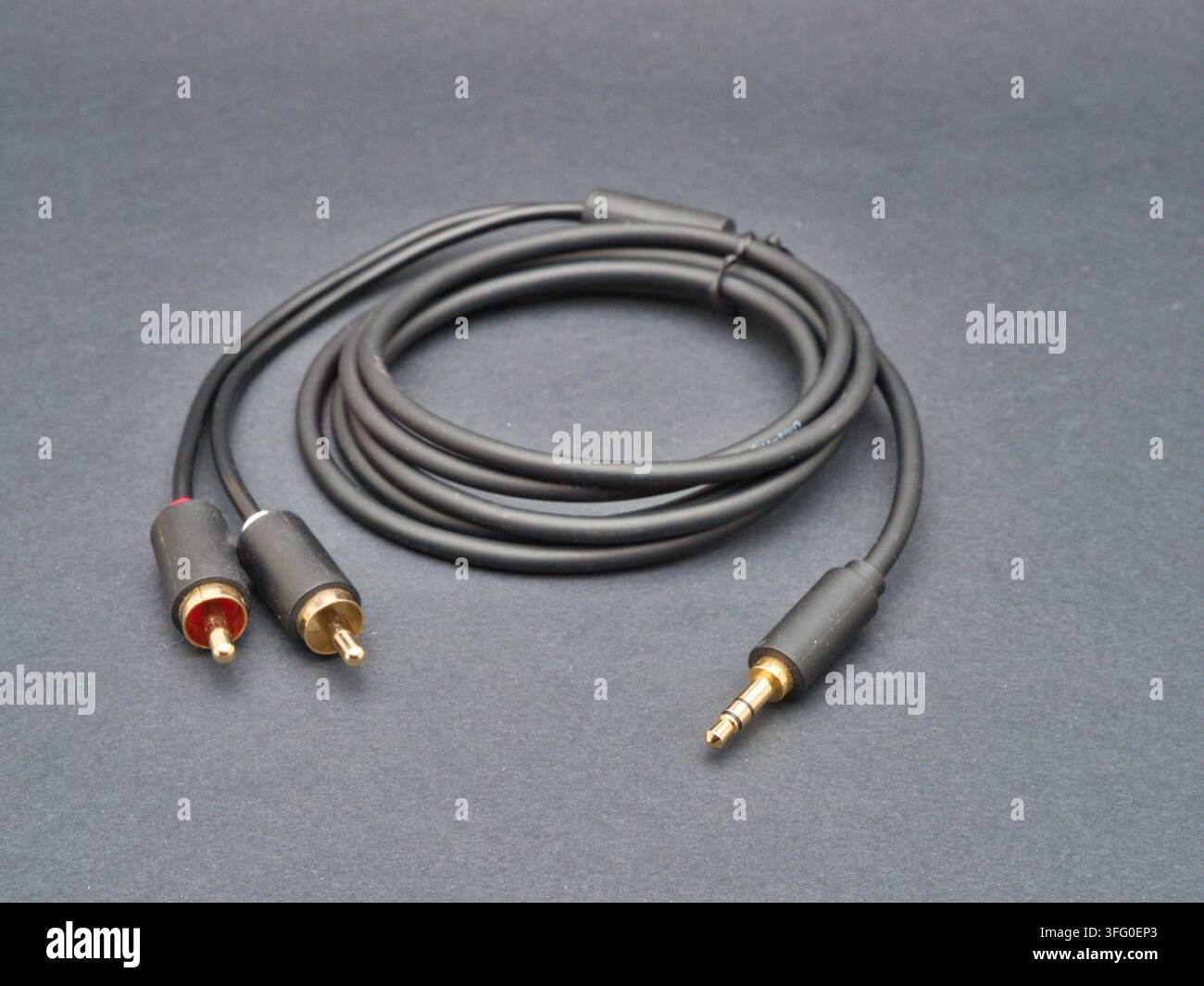 Cavo audio nero RCA a jack 3,5 mm - Un cavo audio nero con connettori RCA placcati in oro su un'estremità e un jack da 3,5 mm sull'altra, arrotolato ordinatamente su un Foto Stock