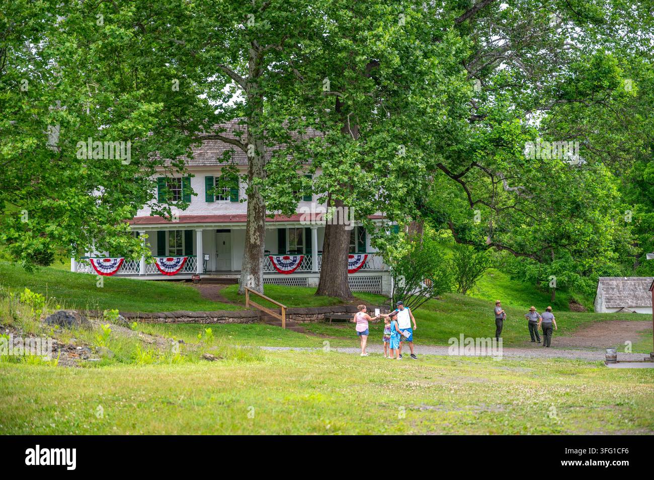 ELVERSON, PA, USA - 06-25-2026: Visitatori e ranger del parco camminano vicino a una casa storica decorata con bandiere americane a Hopewell Furnace National Histor Foto Stock