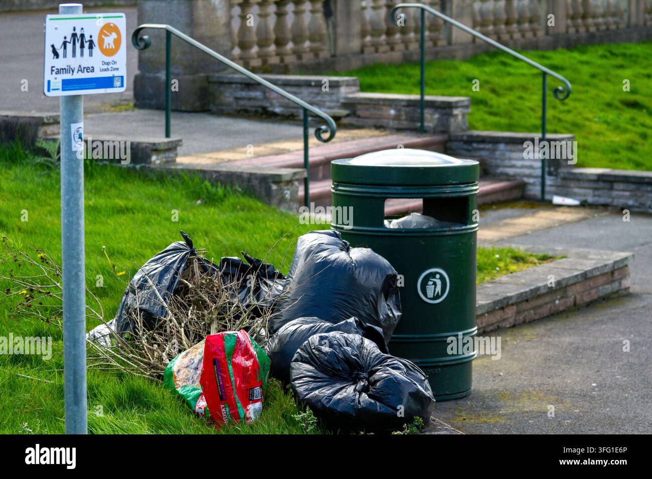 Un mucchio di sacchi della spazzatura, abbandonato su un bordo erboso vicino a un cestino pubblico all'interno di una zona "Area famiglia / Zone per cani al guinzaglio". Southport, Regno Unito. Foto Stock
