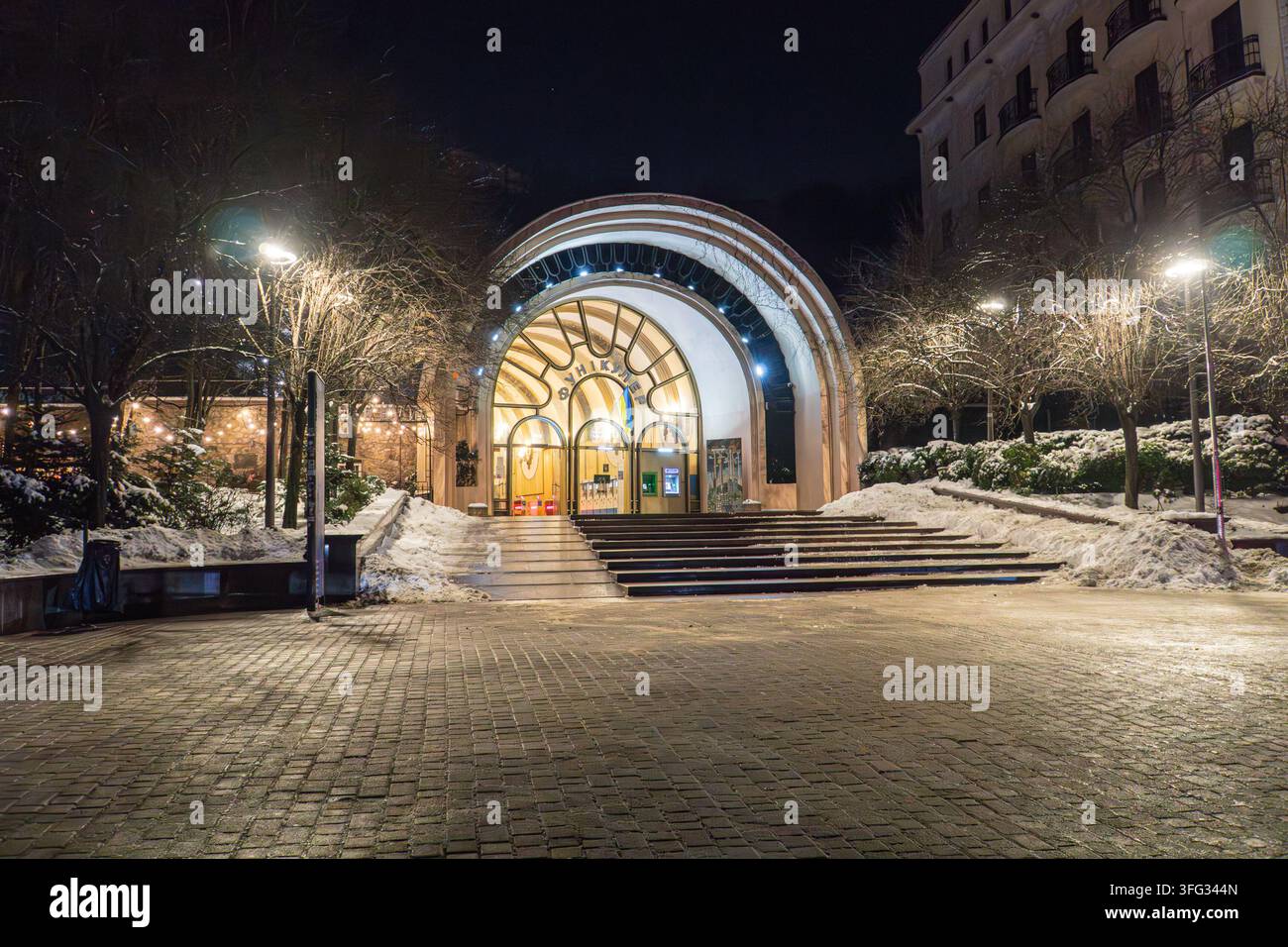 Ingresso moderno e curvo di un edificio funicolare a Kiev, Ucraina durante l'inverno L'illuminazione interna calda contrasta con l'esterno scuro e l'ambiente innevato Foto Stock