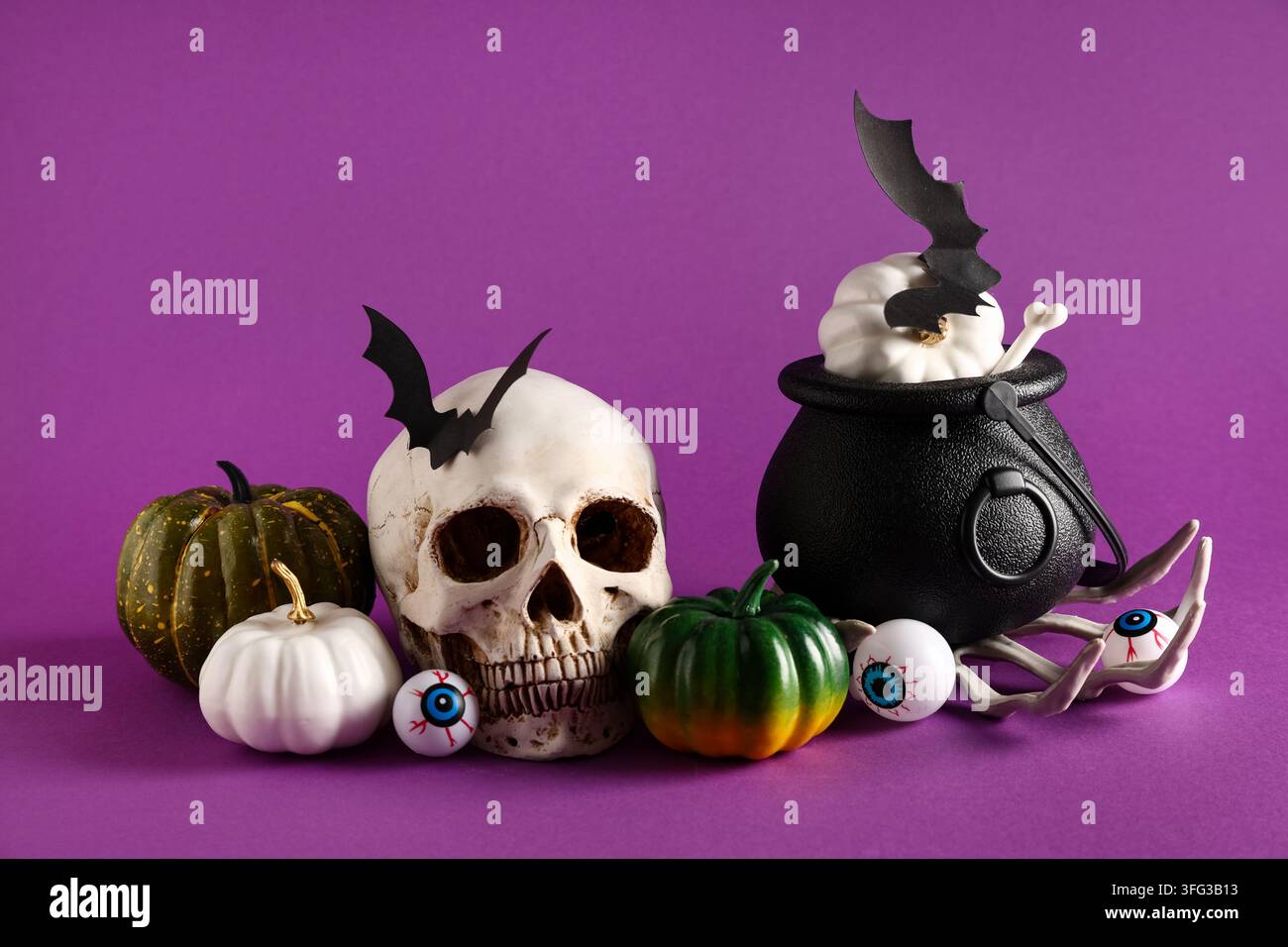 Festa di Halloween e decorazioni spettrali per le feste, teschio umano con zucche e calderone di una strega su sfondo viola per il design di inviti per feste festive Foto Stock
