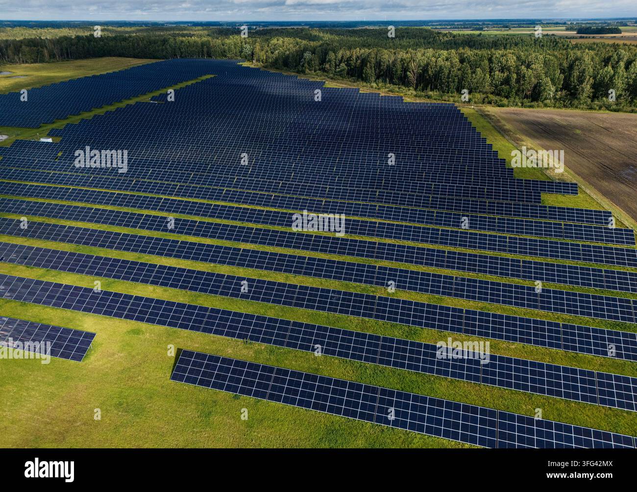 Vista aerea di una vasta fattoria solare su una verde area paesaggistica delimitata da foreste e campi agricoli, energia rinnovabile su larga scala e così Foto Stock