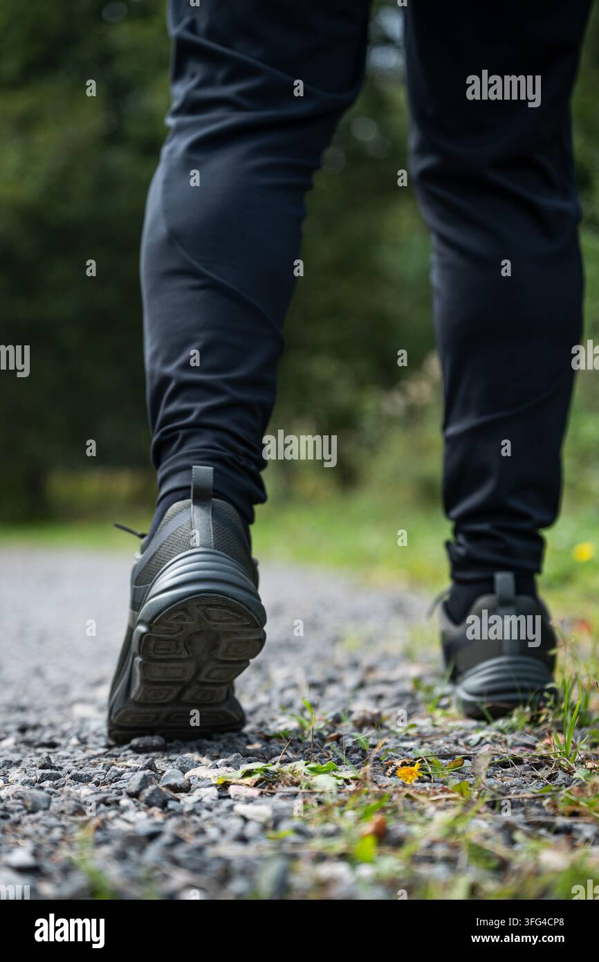 Prima piano vista posteriore di un uomo anziano che cammina su una strada all'aperto con scarpe da ginnastica, promuovendo l'attività quotidiana, la mobilità e l'invecchiamento sano. Formato verticale. Foto Stock