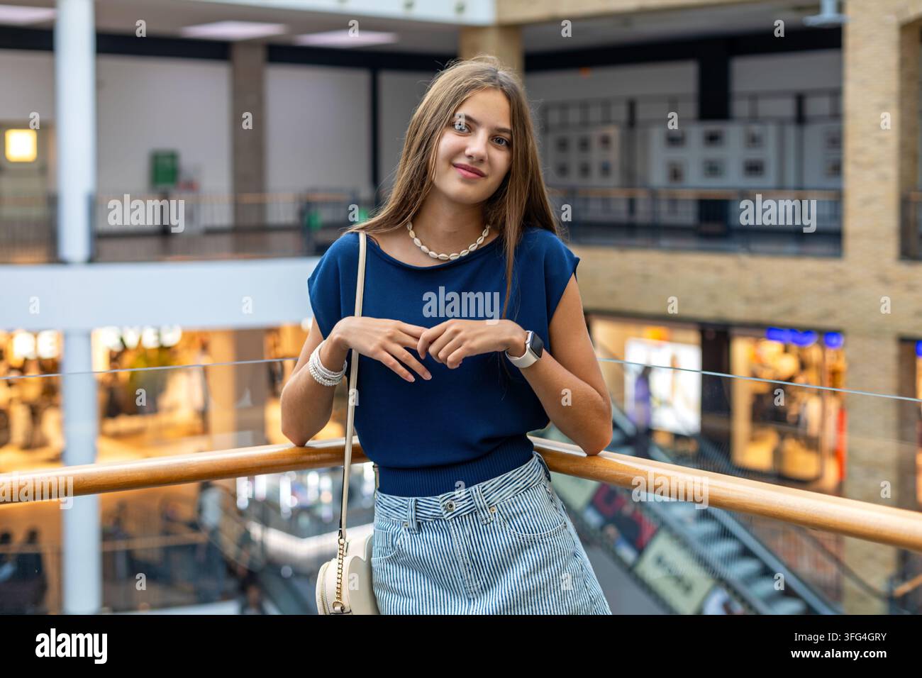 Giovane donna in piedi in un centro commerciale moderno. Giovane donna sorride mentre è in piedi vicino a una ringhiera all'interno di un centro commerciale moderno con negozi e un Foto Stock