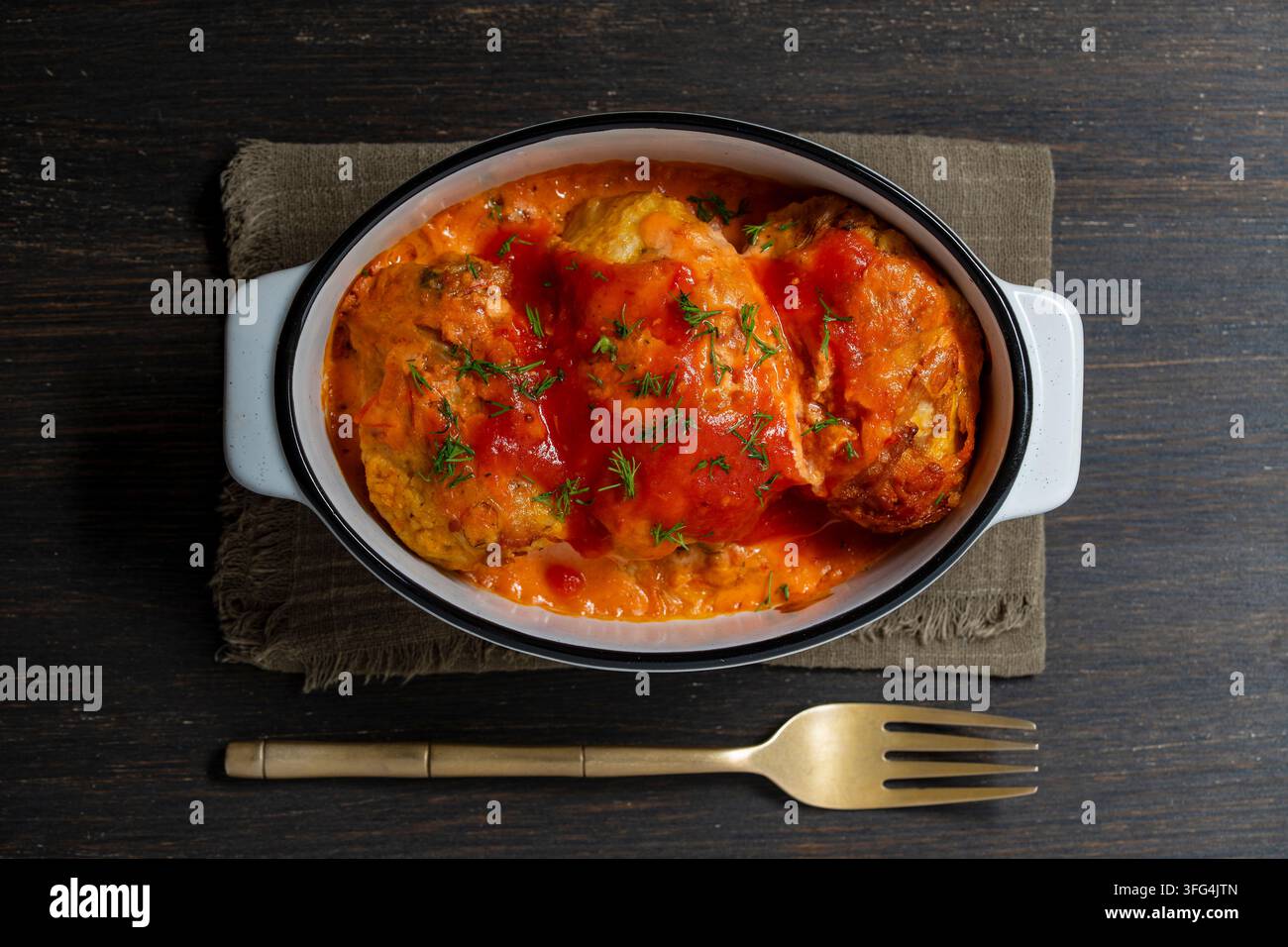 Vista dall'alto di involtini di cavolo fatti in casa in una teglia di ceramica. Tradizionali involtini di cavolo ripieni o golubtsi con salsa di panna al pomodoro e aneto fresco all'interno Foto Stock