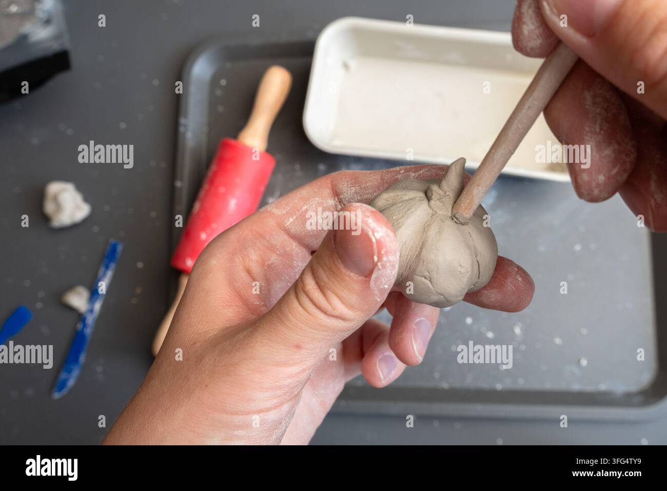 Mano che modella una zucca in miniatura di argilla con uno strumento di modellazione in legno Foto Stock