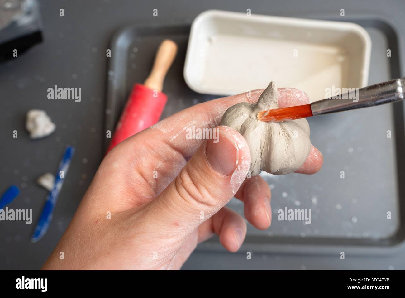 Artista che liscia uno stelo di zucca in argilla fatto a mano con un pennello bagnato Foto Stock